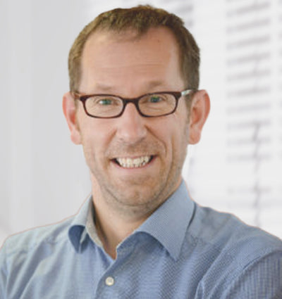 Mann mit Brille und blauem Hemd lacht in die Kamera